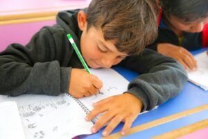 Photo by Salah Darwish Two young boys sitting at a desk writing on paper